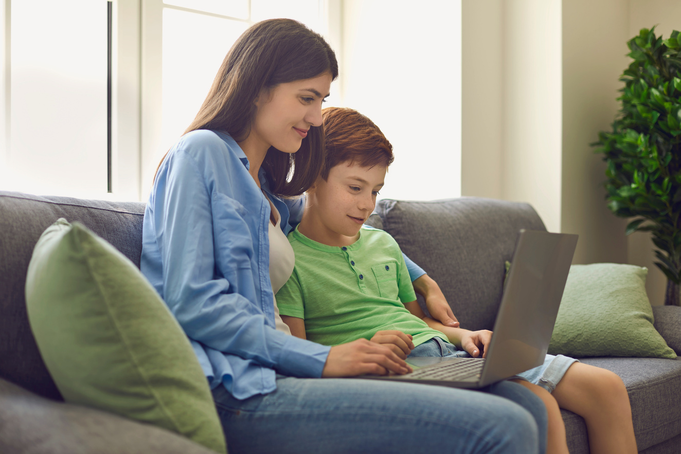 Young Mother and Her Son Talking to Teacher from Home. Parent and Child Watching Online Lesson on Laptop Computer